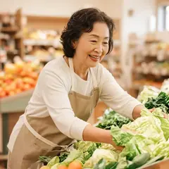 スーパーの売り場で、60代の女性がエプロン姿で野菜を並べているイメージ写真